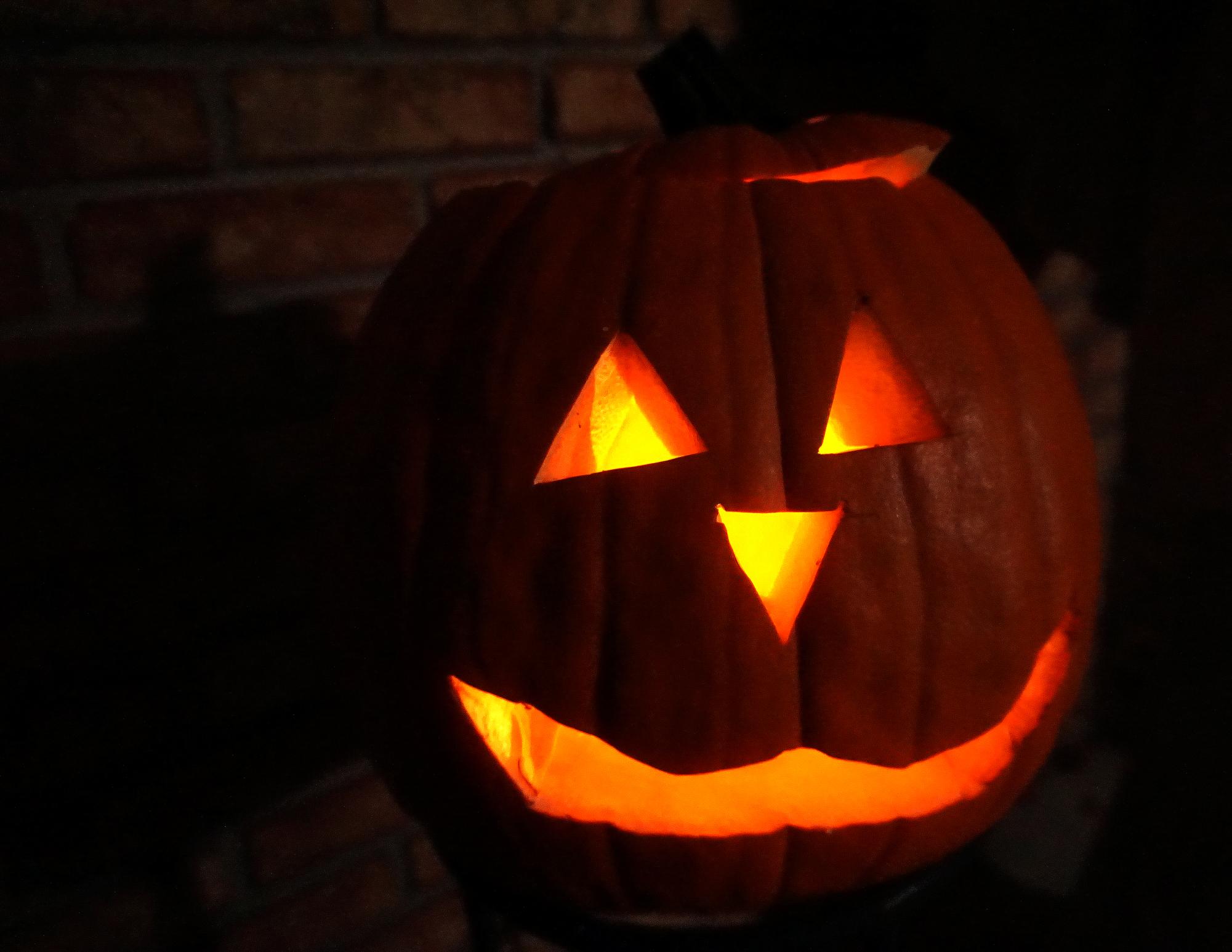 A lit, hand-carved pumpkin, known colloquially as a jack ‘o lantern sits atop a porch stool on Halloween night in celebration of the beloved fall holiday. Oct. 31, 2024