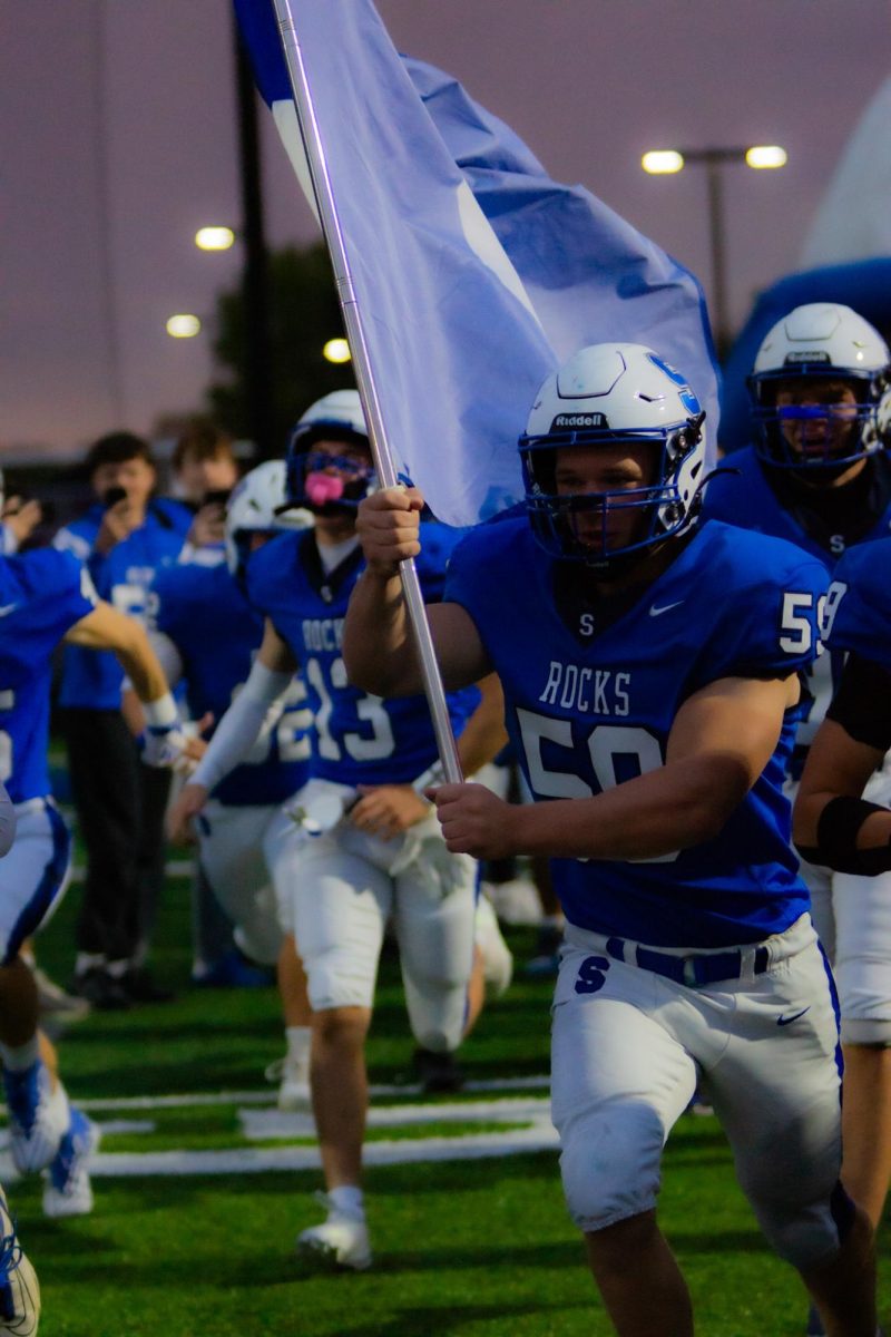 Salem senior Vance Shaw runs onto the field waving the Salem Rocks’ football flag before the homecoming game against Brighton. October 10, 2025.